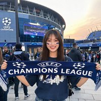 一位年轻女球迷手持欧冠围巾在球场外留影